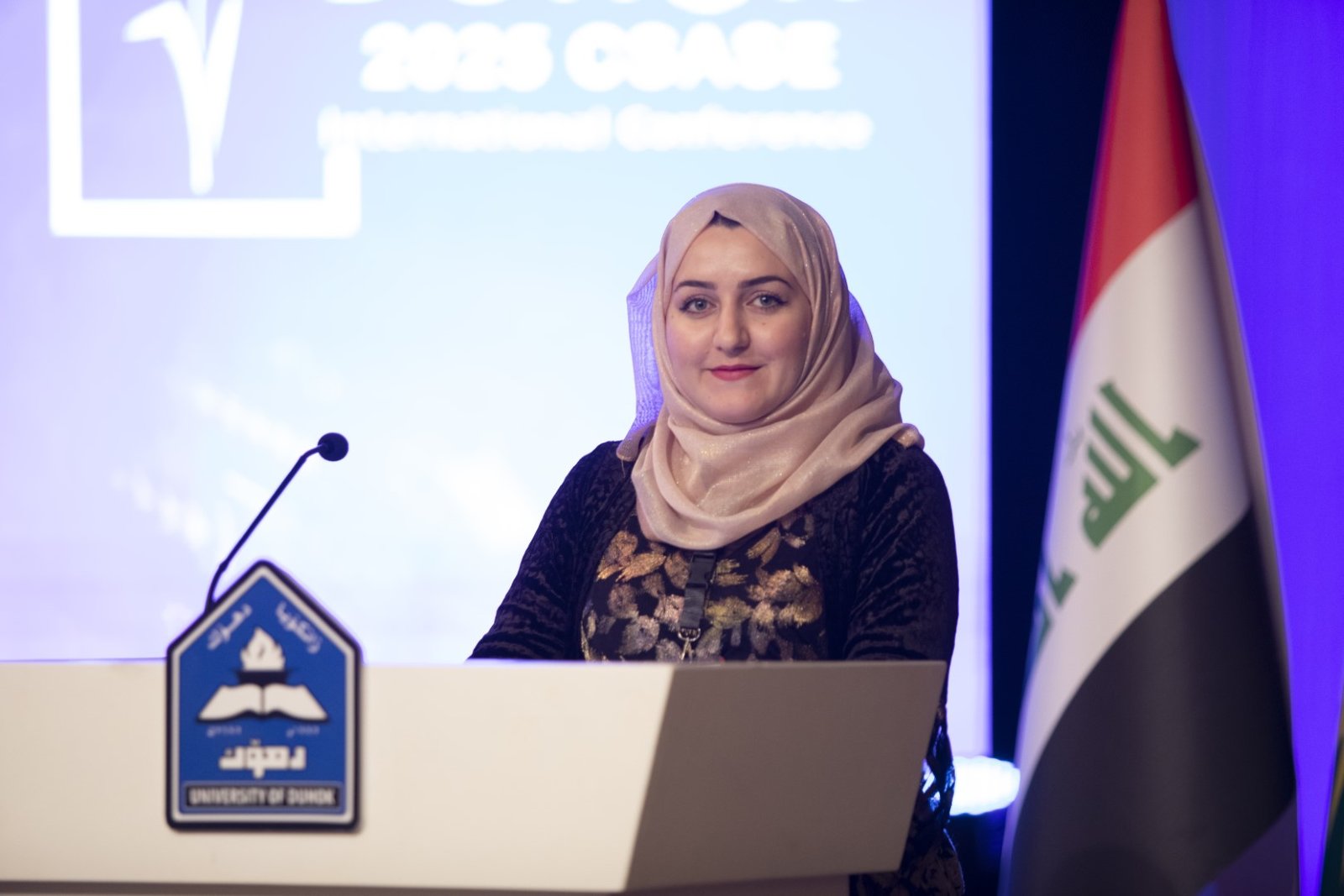 A presenter at the UoD podium with the conference screen behind