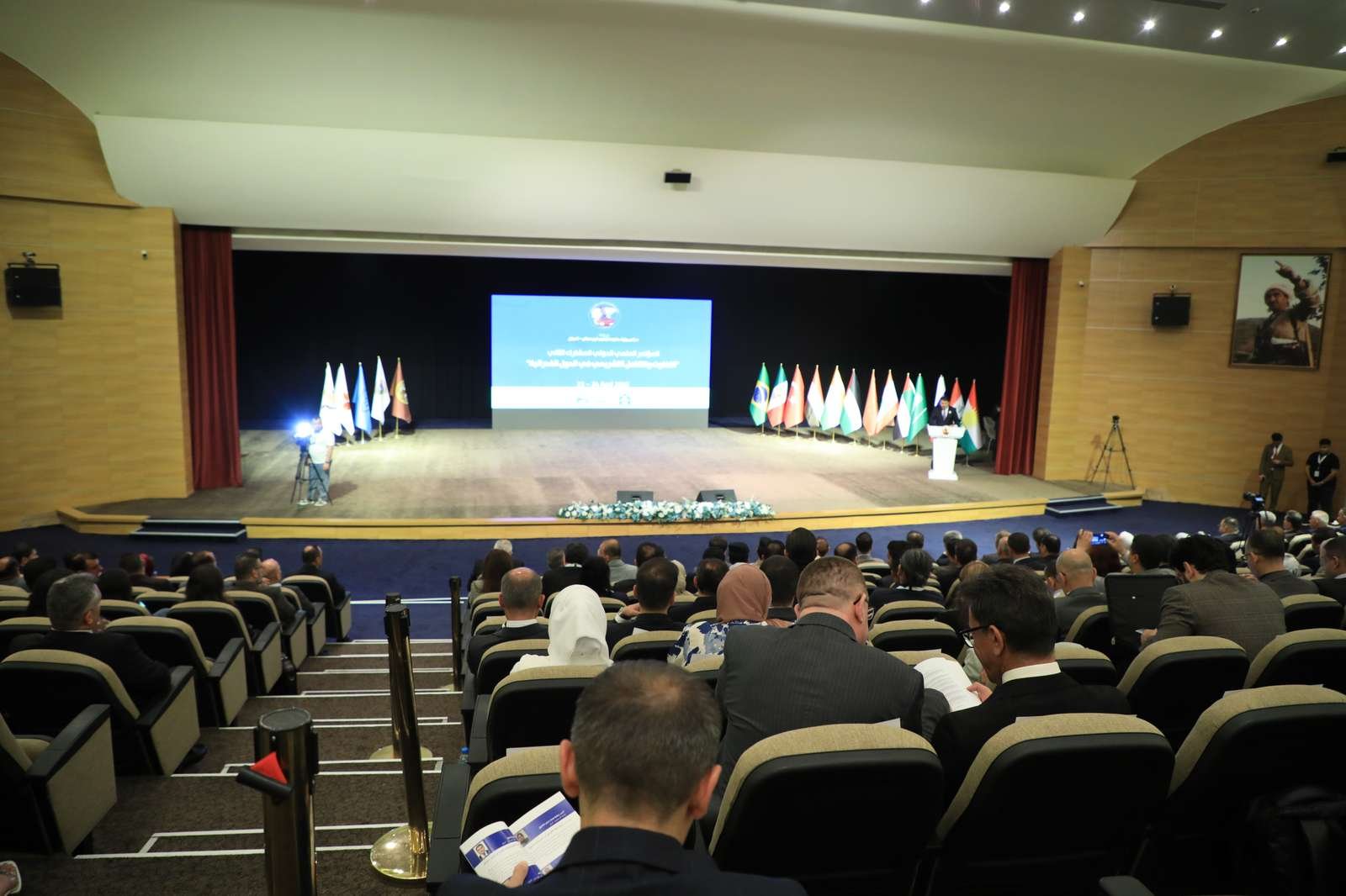 Convention Center hall with flags on stage and the audience seated
